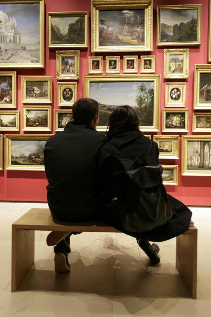 Ein Foto zeigt ein kuschelndes Paar auf einer Bank vor den Gemälden in der Sammlung Daems 