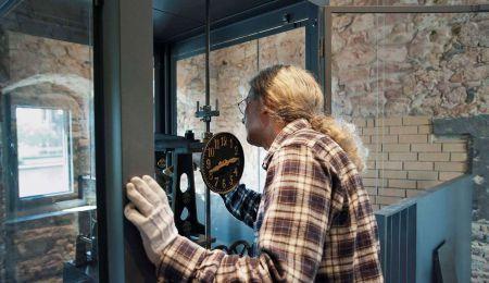 Mann arbeitet an historischer Pendeluhr im Rententurm