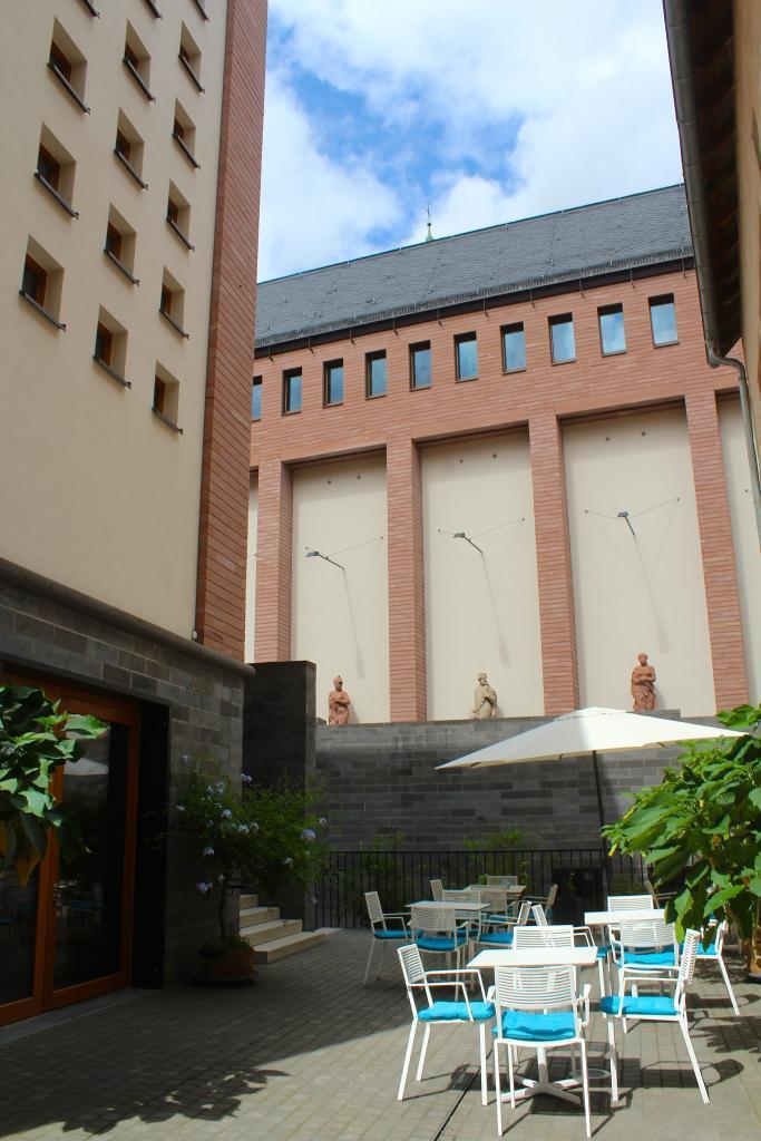Das Foto zeigt den Blick aus dem Innenhof zur Skulpturengalerie, weiße Gartenmöbel, türkise Polster und Pflanzen sind zu sehen. 