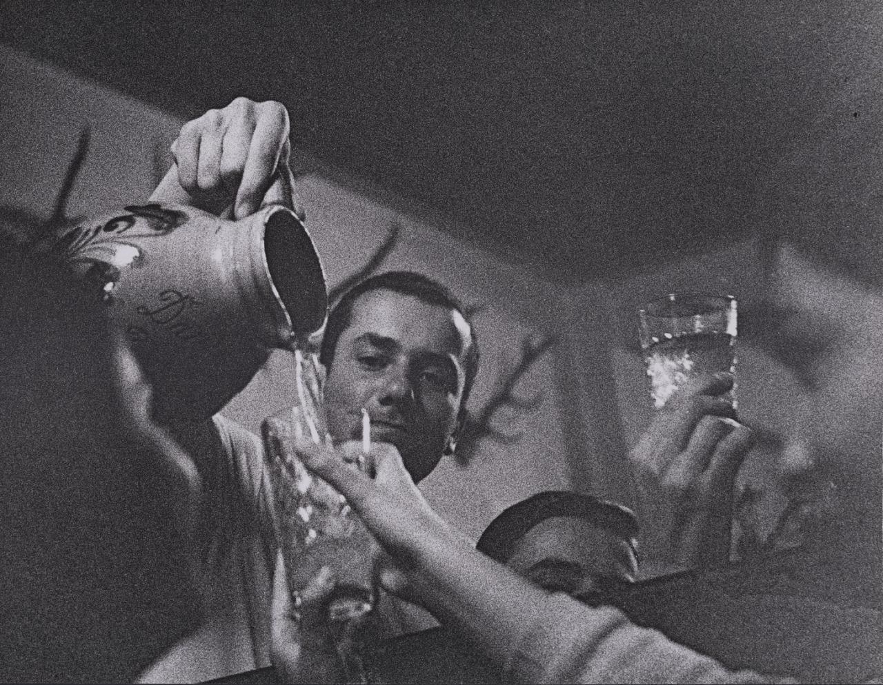 Das Schwarz-Weiß-Foto zeigt einen Mann, der Apfelwein in ein geripptes Glas gießt.